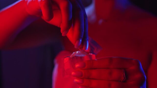 An unidentified adult woman wrapped in a towel and illuminated by neon lights takes a condom out of its packaging to protect herself from sexually transmitted diseases and prevent accidental pregnancy