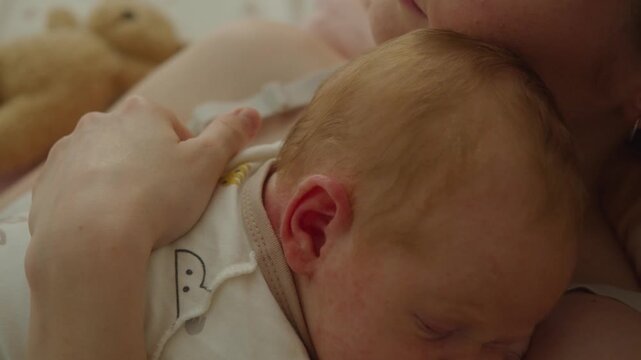 Cinematic shot travels from sleeping baby face toward mother's protective hands. Visual direction shifts attention from vulnerable child to physical support surrounding infant during rest.