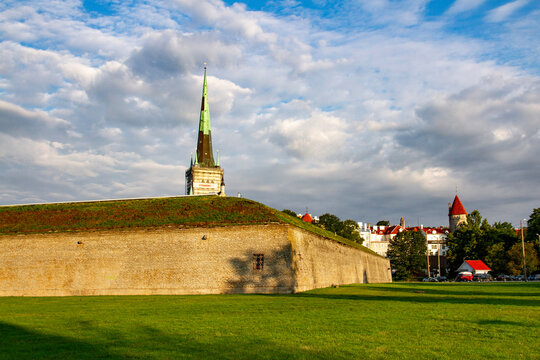 Historic stone bastion of the Little Coastal Gate with St. Olaf's  green spire rising in the background under a peaceful, early morning sky with warm sunlight and white clouds in Tallinn, Estonia