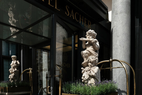 Vienna, Austria - August 18, 2025. Close-up view of the luxury Hotel Sacher entrance, featuring classical cherub stone statues, lavender planters, and elegant golden brass accents.