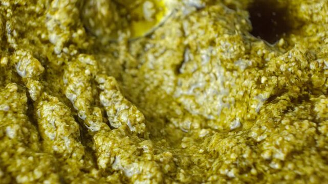 Spoon sliding through thick Italian pesto sauce with olive oil