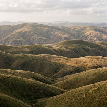Rolling green hills landscape under cloudy sky, scenic mountain range with velvet texture, vast natural valley panorama