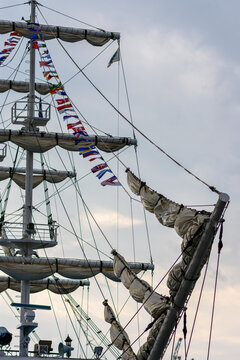A detailed low-angle shot of a traditional sailing vessel's upper section focusing on its complex rigging and sails against an overcast sky