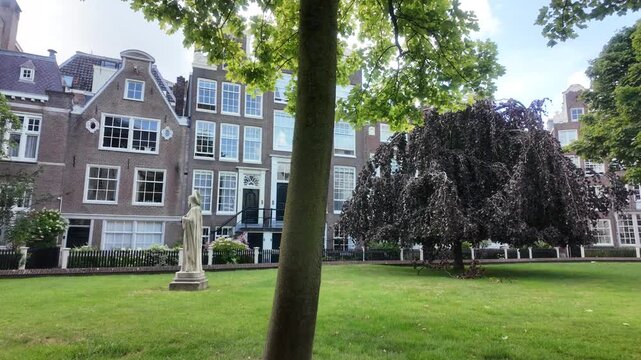 Historic Begijnhof courtyard in Amsterdam with stone statue, green lawn and gabled brick houses