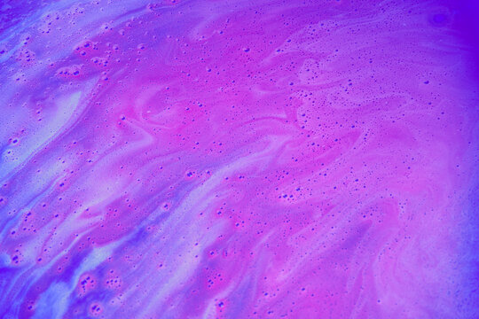 Abstract blue and purple liquid surface with bubbles and flowing foam, creating a vibrant watery texture with swirling patterns.