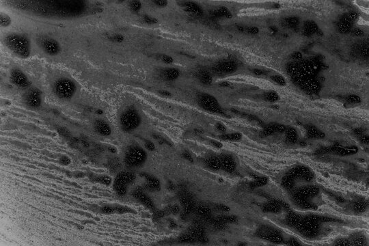 Abstract black liquid surface covered with small bubbles and swirling foam, resembling oil pollution or a chemical spill.