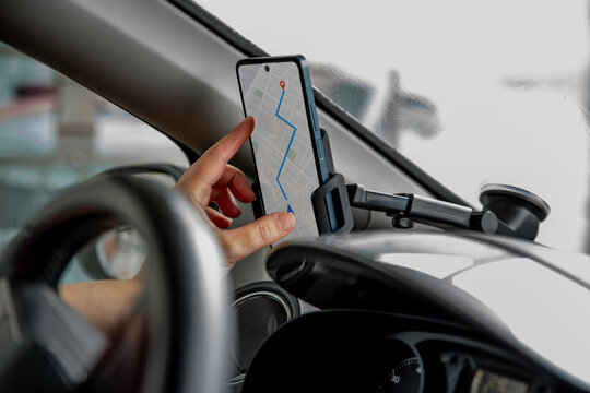 Driver touches a smartphone navigation map mounted beside the steering wheel while traveling. Hand using a mobile GPS application on a phone holder inside a car