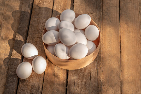 Chicken eggs in wooden bowl on grunge table in chicken coop, barn. Countryside outdoor setting in the backyard