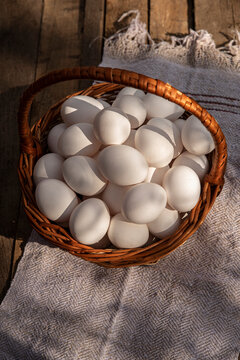 Chicken eggs in a wicker large basket on wooden grunge table. Countryside outdoor setting