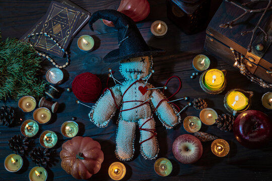 Witch wizard witchcrafting, performing ritual with handmade voodoo doll among candles, pumpkins. Magician Halloween night