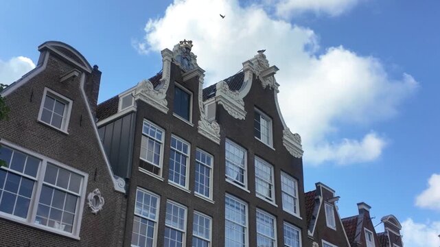 Ornate bell-shaped gables with statue and crown on traditional Amsterdam canal houses against blue sky