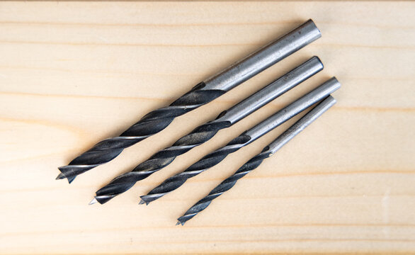 Used wood drill bits for a drill lying on a wooden board, view from above. Tools and equipment for woodworking and carpentry used by DIY enthusiasts, tradespeople, and in industry.