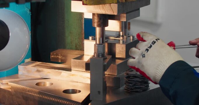 Skilled machine operator performs repetitive production tasks on punch press workstation. Industrial labor shown in close-up
