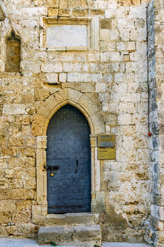 Medieval arched wooden door set in ancient stone wall in Rhodes old town