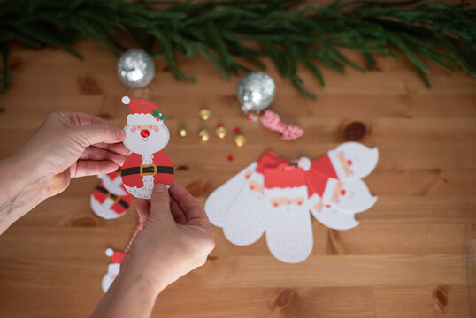 Hands assembling Santa Claus paper decorations on wooden table with ornaments