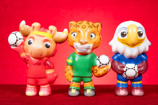 ZhongShan GuangDong China-November 5 2025: Three soccer themed mascot toy figurines holding footballs arranged on red backdrop.