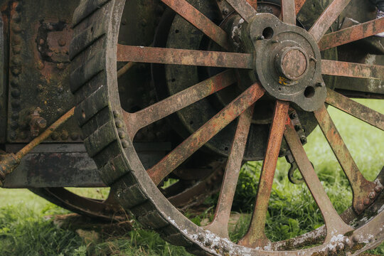 Rusty vintage agricultural machinery wheel with wooden spokes and metal rim resting on green grass in an outdoor setting