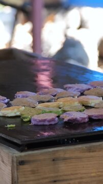 Vertical video. Street food vendor preparing traditional Thai coconut pancakes called Khanom Babin on a hot griddle at a market stall