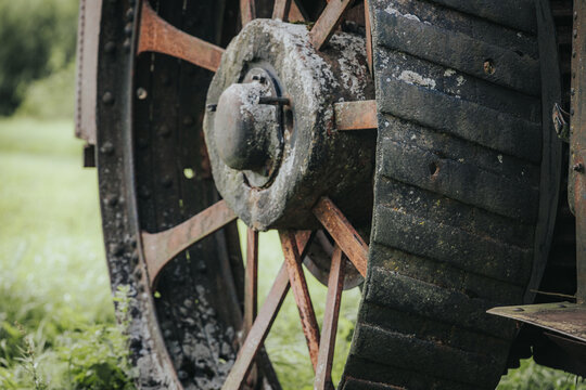 Close-up view of an antique tractor wheel showcasing rusted metal and worn rubber tread against a blurred green field background