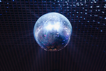 Fototapeta premium disco ball with mirror surface and bright rays, blue light, hanging on ceiling, night party background