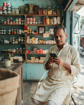 Middleaged indian shopkeeper using a smartphone in his small grocery store