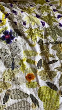 An eco print in progress on crumpled white fabric, revealing natural green leaves and vibrant purple and orange botanical dye imprints.