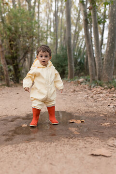 Child wearing raincoat and boots playing in autumn puddle