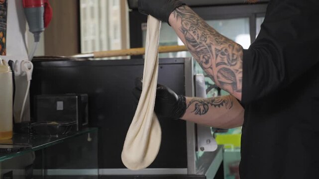 Close-up of a chef in gloves, rolling out the dough with his hands and shaping it into a pizza. The pizzeria chef kneads the corn flour dough for pizza.