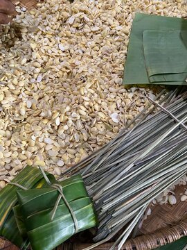 Handmade tempe parcels in progress, tightly wrapped in green banana leaves and secured with bamboo sticks alongside peeled soybeans and traditional tools.
