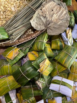 Handmade tempe parcels in progress, tightly wrapped in green banana leaves and secured with bamboo sticks alongside peeled soybeans and traditional tools.