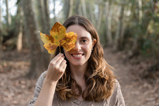 Woman smiling holding autumn leaf covering eye