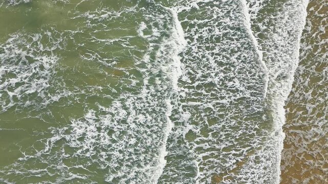 Aerial top down view of wave with foam patterns along sandy shoreline. Abstract sea texture background