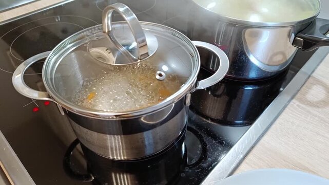 Boiling pots on ceramic cooktop with glass lids shows meal preparation at home with european man checking boiling pots lid with steam and delicious vegetables as healthy meal cooking at home.