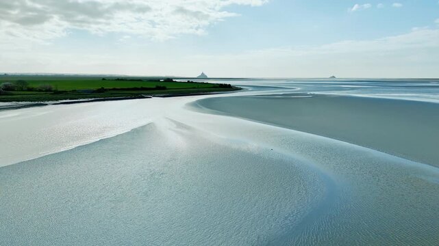 Drone footage of Normandy tidal landscape at low tide, exposed sand and reflective wet surfaces