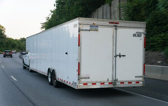 Pennsylvania, U.S.A - Jul 11, 2026 - A white Car Mate enclosed trailer with dual axles towed by pickup truck on highway.