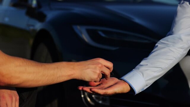 Male hand giving key of car to buyer of electric automobile outdoor. Handshake between salesman and new owner of modern auto after successful deal. Concept of buy or rent car. Slow mo