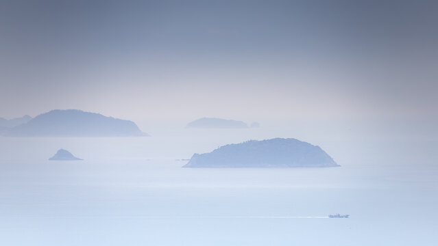 Minimalist Ink Wash Style Landscape of Misty Islands and Solitary Boat Sailing Across Hazy Calm Sea in Dadohaehaesang National Park, South Korea