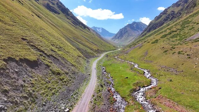 Cyclist on the mountain road in narrow valley between snow peaked mountains. Girl on a walk in countryside. Scenic landscape, vivid colors. Outdoor activity and healthy lifestyle concept.