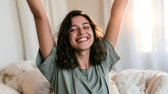 Joyful happy woman stretching arms in bed morning, cheerful smiling girl waking up relaxed, bright cozy bedroom wellness