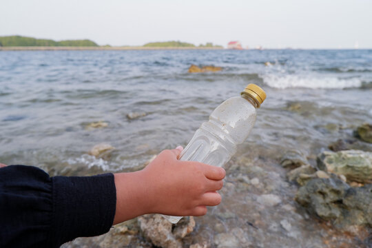 Hand picking up discarded plastic bottle on ocean shore for beach cleanup and environmental conservation