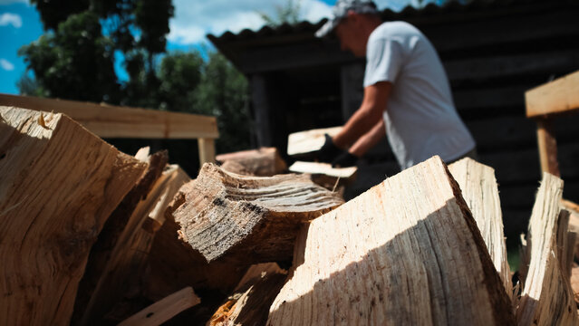 Man wearing protective gloves stacking split wooden logs onto rack preparing firewood in backyard