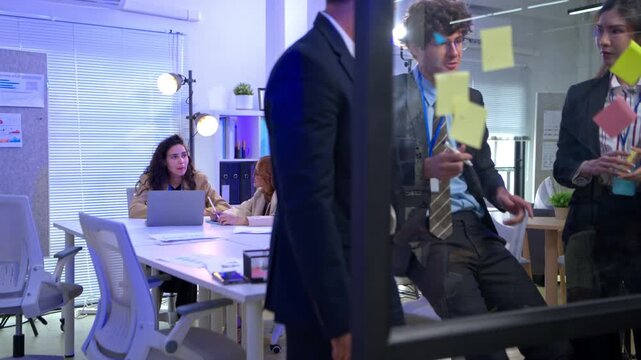 Group of business people presenting reports and brainstorming project information and writing on a glass whiteboard during a professional meeting in a modern office