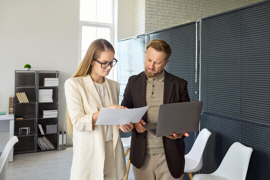 Analyst businesswoman and manager review data reports. In an office they discuss analysis and teamwork checking a report on a laptop in a meeting. Clear concept of teamwork and discussion.