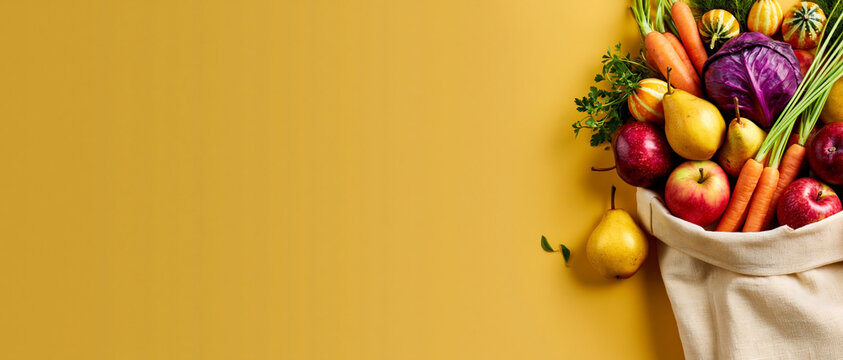 Autumn harvest bag with apples, pears, carrots, pumpkins and red cabbage on yellow background with copy space