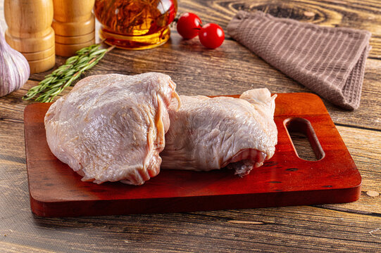 Raw chicken thighs on wooden cutting board with herbs and spices