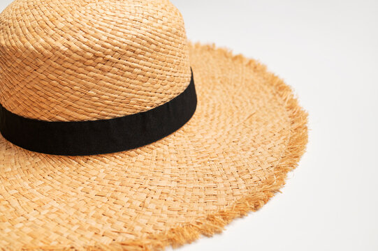 Straw sun hat on white background viewed from above, featuring wide frayed brim and black band. Summer headwear suits beach styling, vacation campaigns, travel content and seasonal fashion