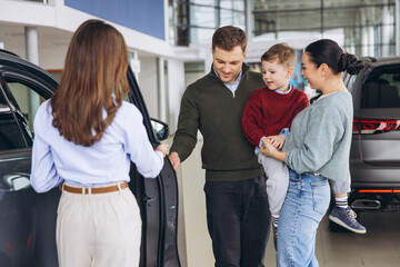 Obraz premium Happy family with child looking at new car with saleswoman in auto showroom, making purchasing decision