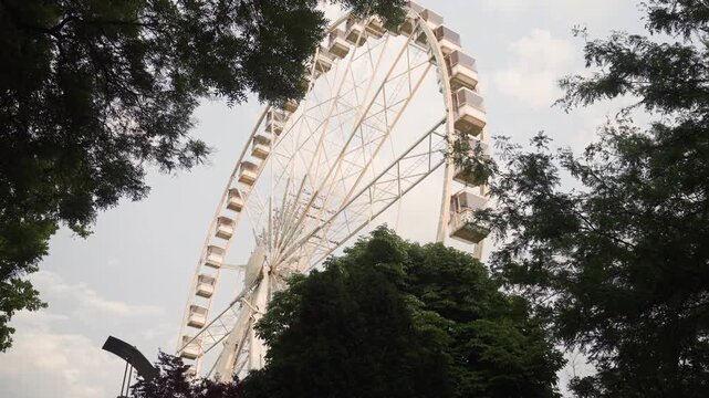 Spinning Budapest Eye Ferris wheel behind green trees in city park
