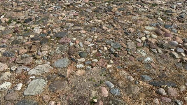 Rocky ground surface with various sized stones and pebbles in gray, pink, brown colors, natural texture background, beach or riverbed