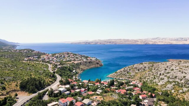 Aerial view of a coastal village near blue sea, rocky hills and winding road